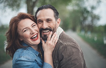 Older couple with dental implants in Houston smiling outside