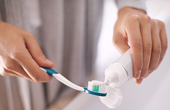 Hands spreading toothpaste onto toothbrush