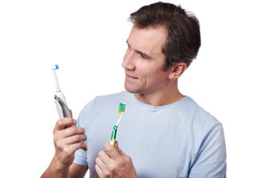A man holding an electric and a regular toothbrush in each hand
