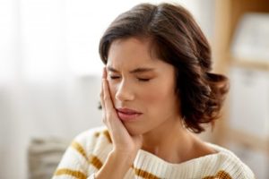 Woman with her eyes closed is holding her cheek with her hand 