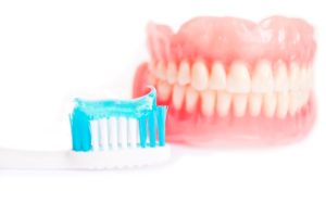 in the background a set of dentures with a toothbrush and toothpaste in the foreground